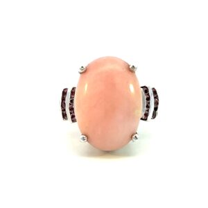 One estate sterling silver faux coral and pink tourmaline ring containing an 18x13mm oval cabochon faux pink coral in a four-prong setting. Each shoulder of the ring features 2 vertical channel settings, the first set with 4 pink tourmaline and the second set with 3 pink tourmaline. The pink tourmalines are round-faceted and measures 1.5mm each.
