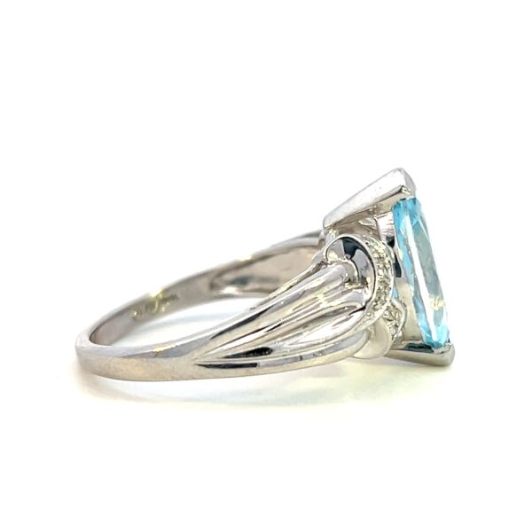 One estate blue topaz and diamond ring crafted from 10 karat white gold with a center marquise blue topaz measuring 13x6mm and 10 round brilliant diamonds set in the band in an "X" design that appears to cradle the center topaz.