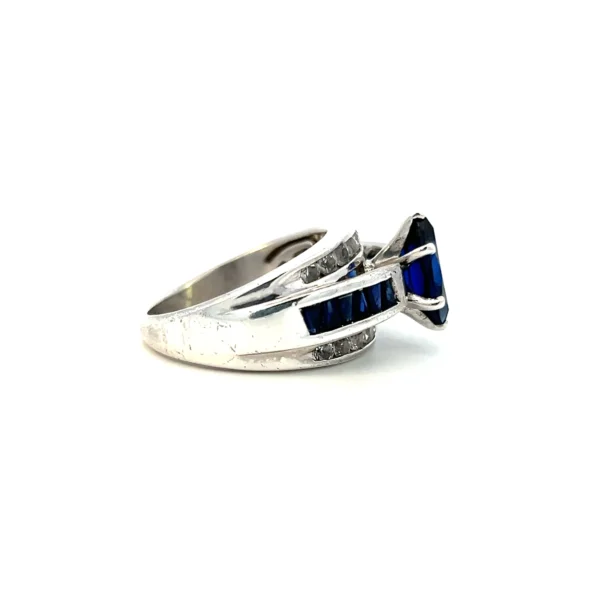 One Estate Lab-Created Blue Sapphire and Diamond Ring crafted from sterling silver with a raised center row set with a center lab-created marquise blue sapphire with 12 lab-created triangle-shaped blue sapphires in a channel settings in the band. The top and bottom rows of the band span the entire front and feature 18 round white sapphires