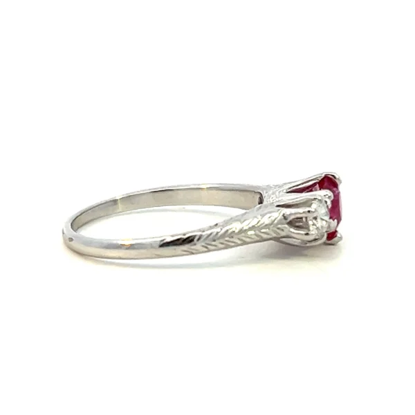 One (1) antique estate 14 karat white three-stone gold ring from 1925 set with a center round faceted 5mm natural ruby and two old mine-cut diamonds weighing 0.50 total carat weight with matching H/I color and I1 clarity. The band is partially accented by an etched wheat leaf design.