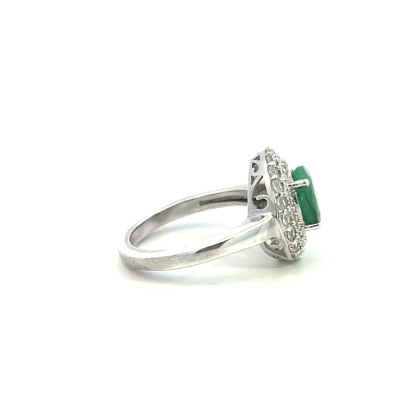 One estate sterling silver fashion ring containing a center oval-shaped faceted emerald measuring 9x7 in a four-prong setting with a slightly open halo design of a very thin milgrain inner halo followed an outer halo of 20 round-faceted white sapphires. Contemporary time period.