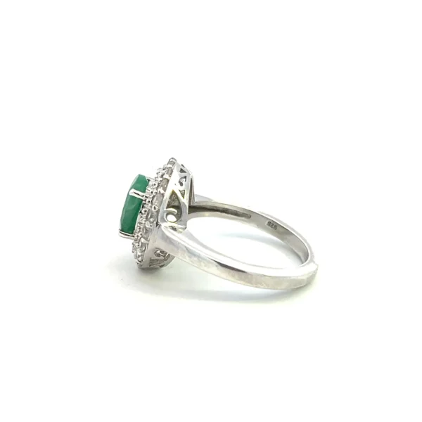 One estate sterling silver fashion ring containing a center oval-shaped faceted emerald measuring 9x7 in a four-prong setting with a slightly open halo design of a very thin milgrain inner halo followed an outer halo of 20 round-faceted white sapphires. Contemporary time period.