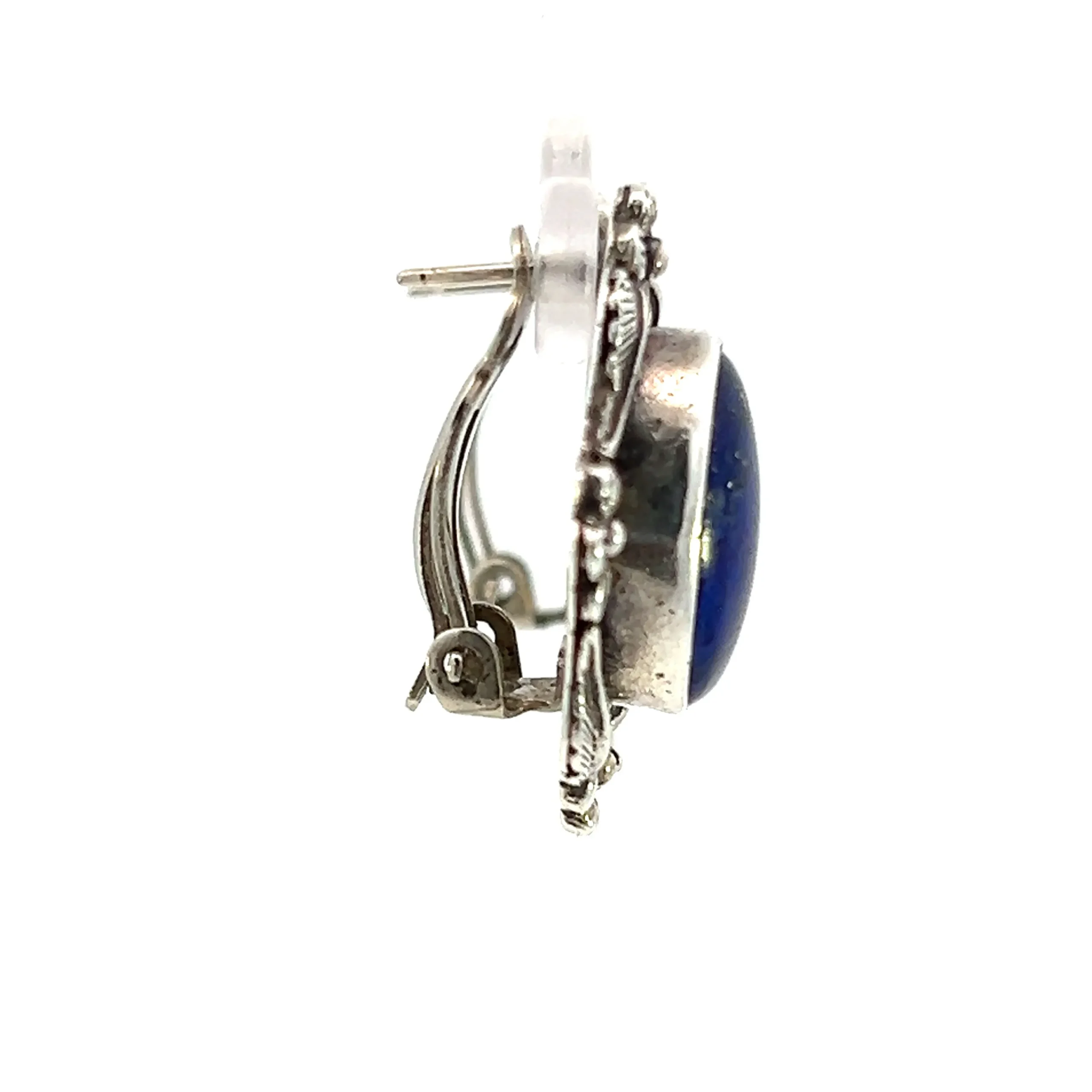 One estate vintage pair of sterling silver stud earrings containing oval cabochon lapis lazuli in a bezel setting surrounded by a curving frame with silver flower accents at each cardinal point. The earrings are secured with omega style backs. Each earring measures 28x25mm.