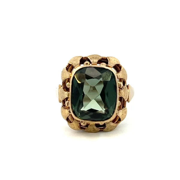 One estate 8 karat yellow gold gemstone ring containing a cushion-cut synthetic green spinel measuring 12x12.5mm in a bezel setting surrounded by an open-work gold frame. The entire top of the ring measures 18x17.5mm. Stamped "333" with a total weight of 4.23 grams. Vintage from the 1930s.