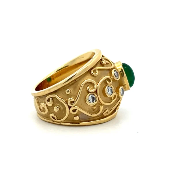 One estate 8 karat yellow gold emerald and diamond ring set with one (1) oval cabochon emerald weighing approximately 0.95 carat and eight (8) round brilliant diamonds weighing 0.30 total carat weight with matching J color and I1/2 clarity. The band is wide and tapers as it goes to the back. The band has a sandblasted finish and raised polished elements including a line along the top and bottom, scroll elements, and the bezel settings for the center emerald and the diamonds. The stones go approximately halfway around the band while the scroll elements go almost entirely around the band.